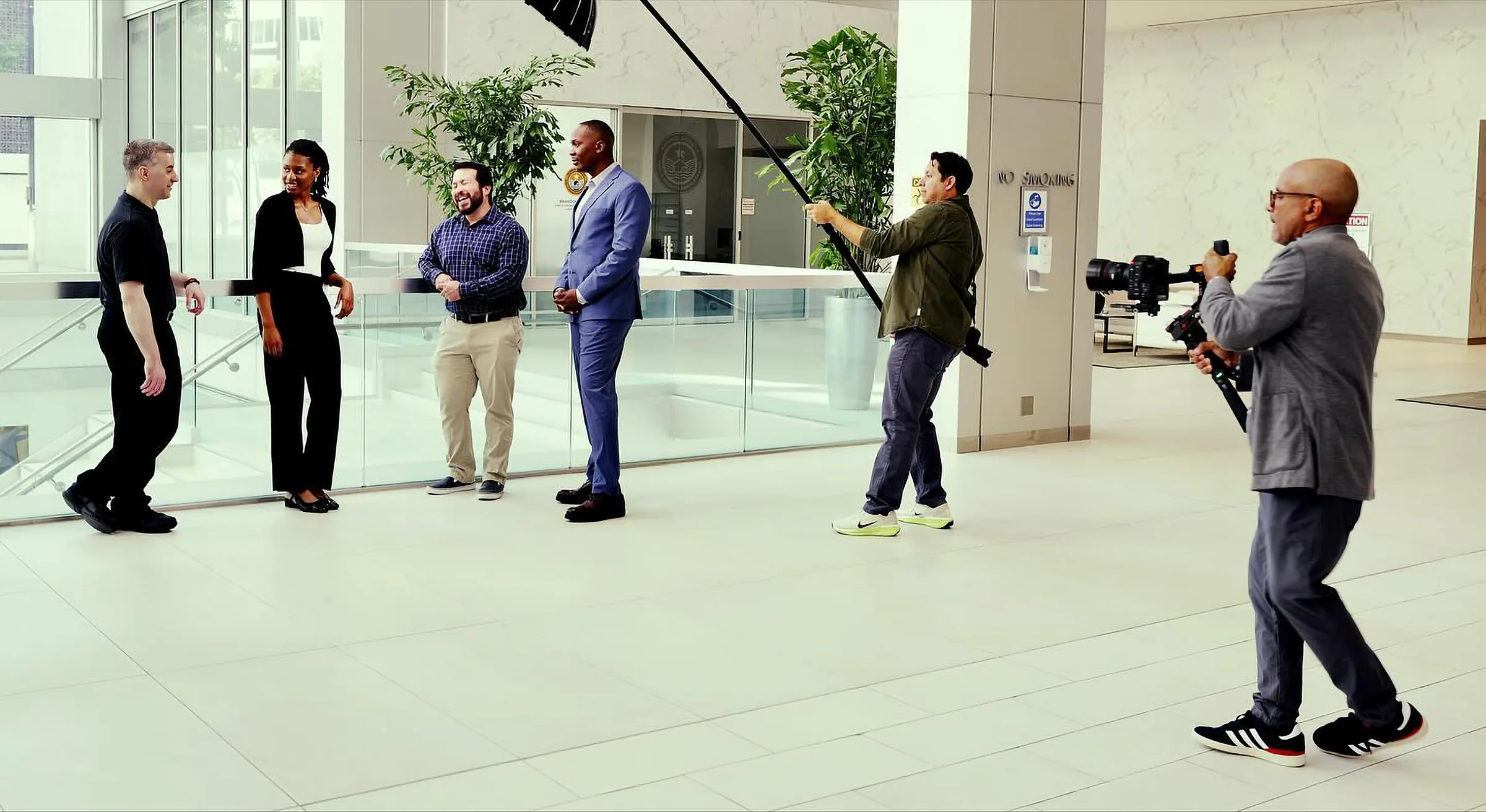 De izquierda a derecha, Charles Williams, Faith Uzo-Onwumere, Justin Gutierrez y Ronald Ndawula platican junto a un barandal de vidrio en el luminoso lobby de unas oficinas en Houston, mientras un microfonista y un operador de gimbal los graban.