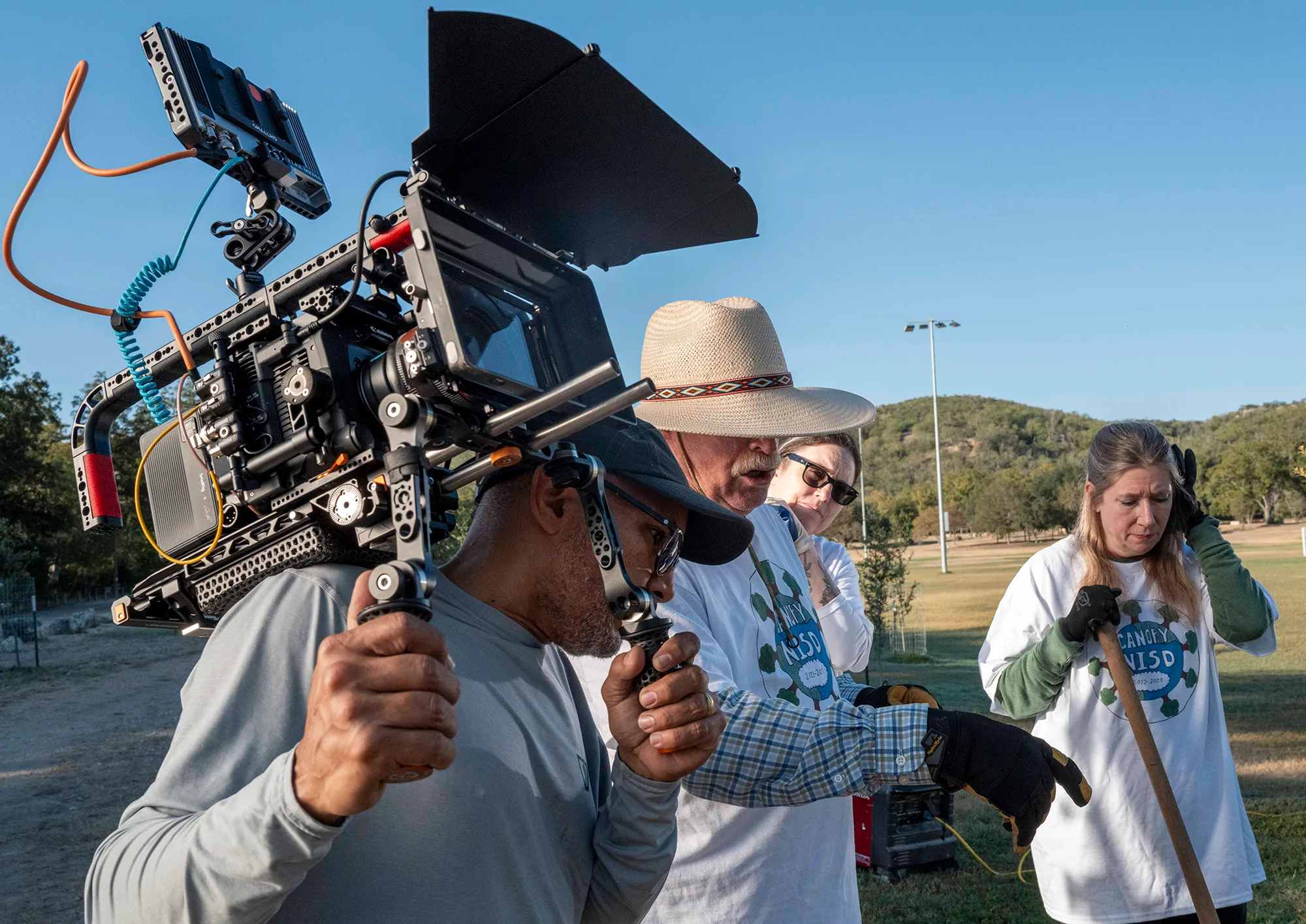 Carlos Javier Sanchez, with a camera on a shoulder rig, films volunteers in Canopy NISD shirts at a tree planting.