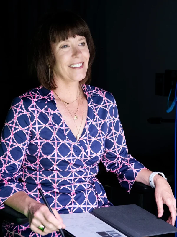 Steffi Ockenfels, executive producer at pixelreflex MEDIA, smiles from her seat on set with a pen and notes in hand.