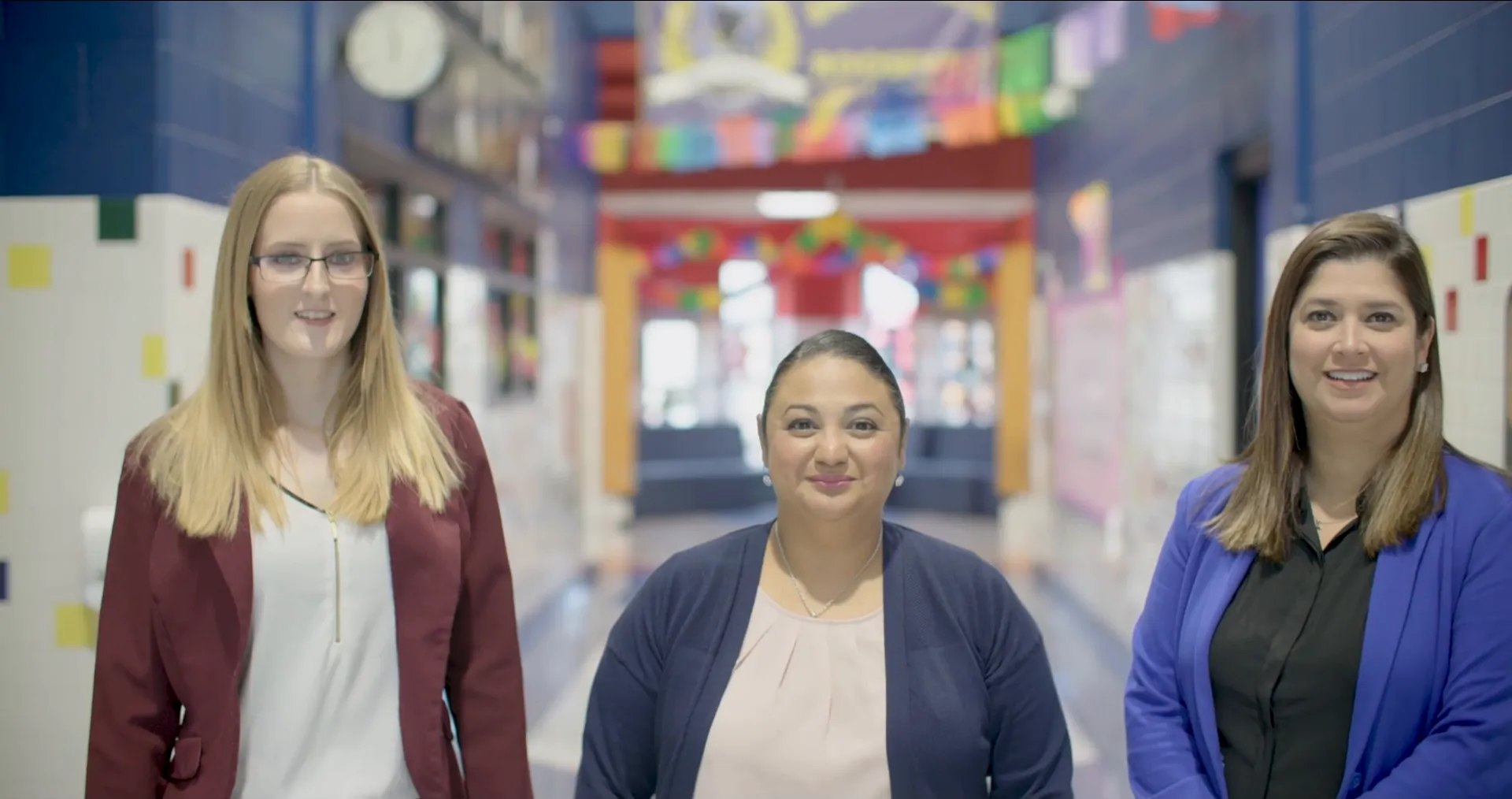 Three Edgewood ISD educators smile in a brightly decorated school hallway.