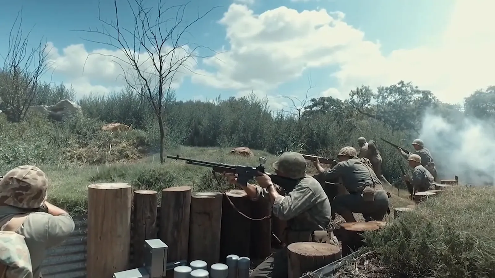 World War II reenactors fire from a log-lined trench as smoke drifts, from our National Museum of the Pacific War video.