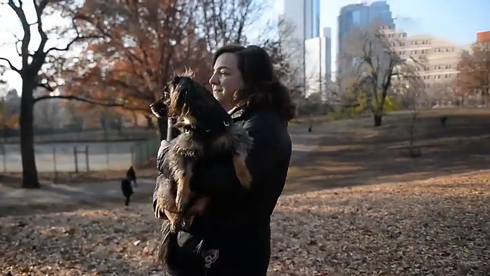 A woman holds her adopted dog in an autumn park with city towers behind her, from our Petco Love adoption story.