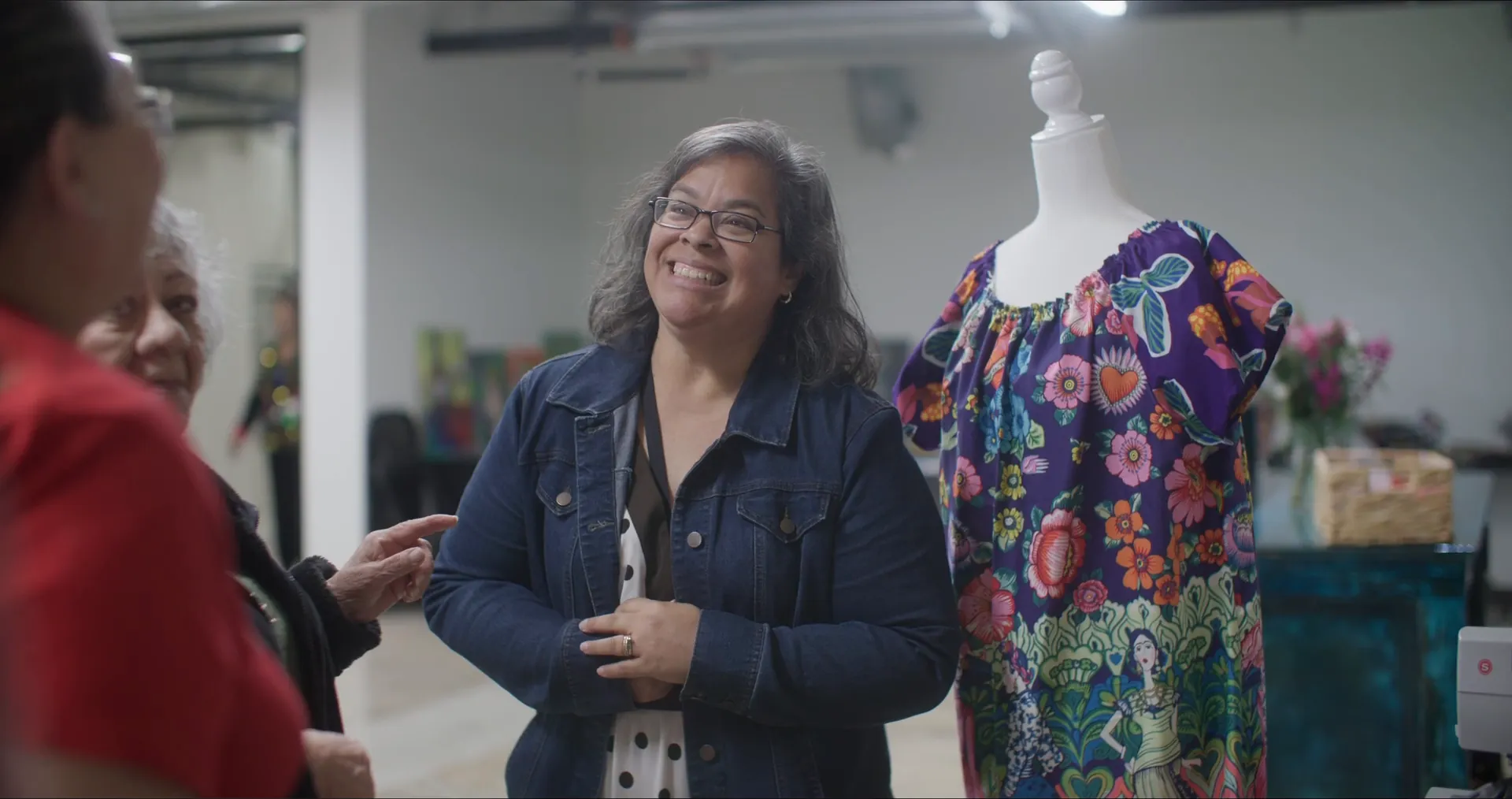 A woman in a denim jacket laughs beside a dress form at Basila Frocks, from our Power of Preservation award video.