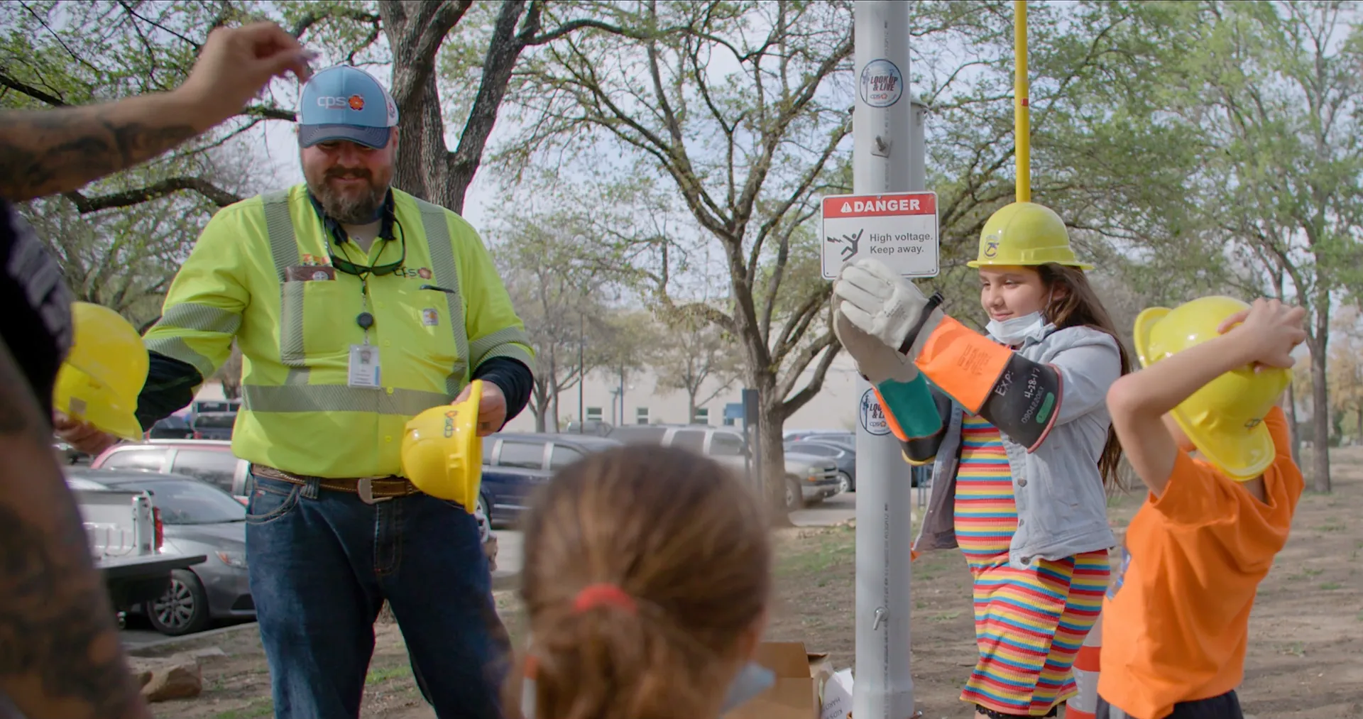 A utility lineworker helps children in yellow hard hats try on safety gear at a Smart Energy Education career day.