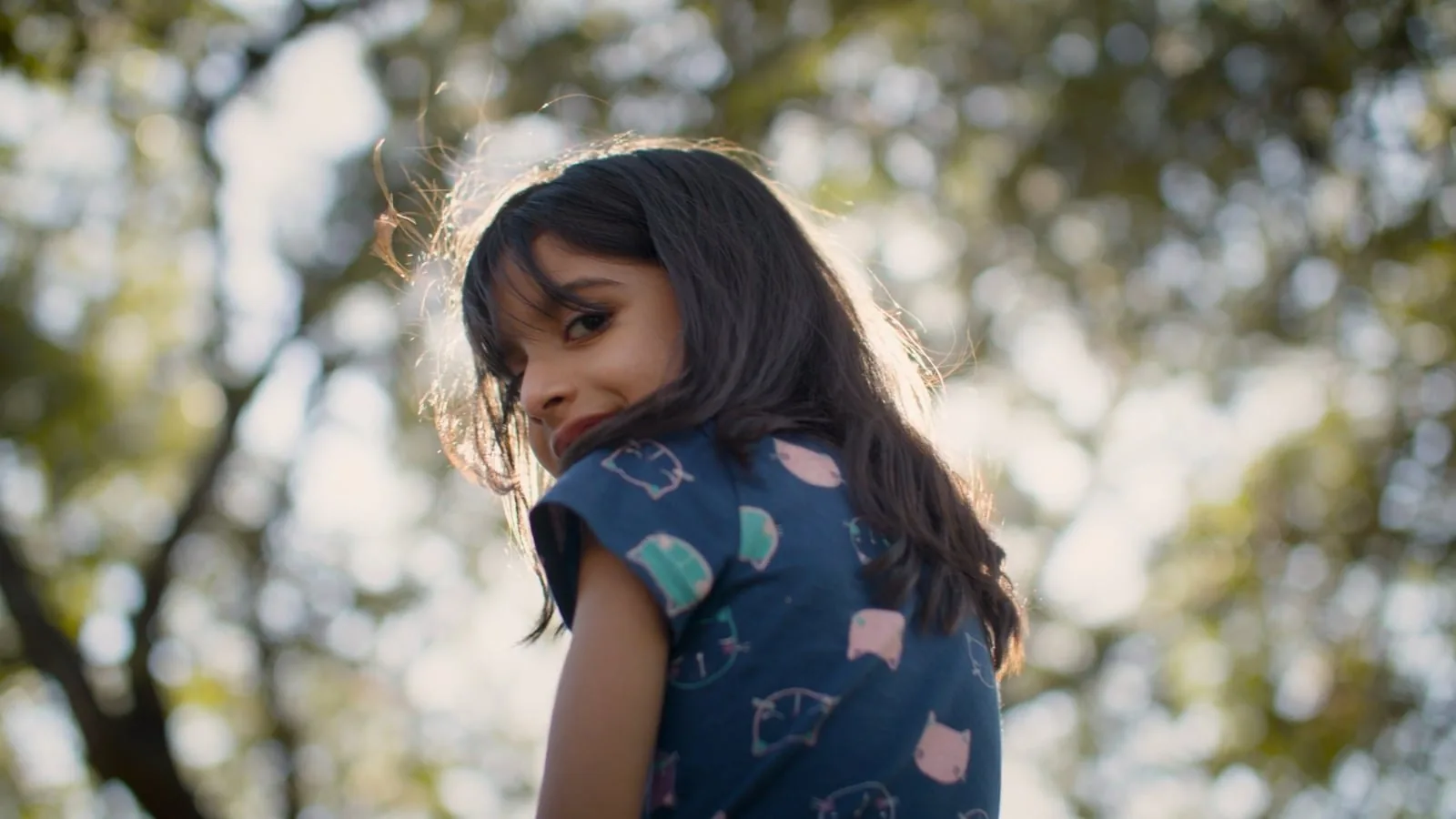A girl smiles back over her shoulder under a tree, a moment from a SAMMinistries client story.