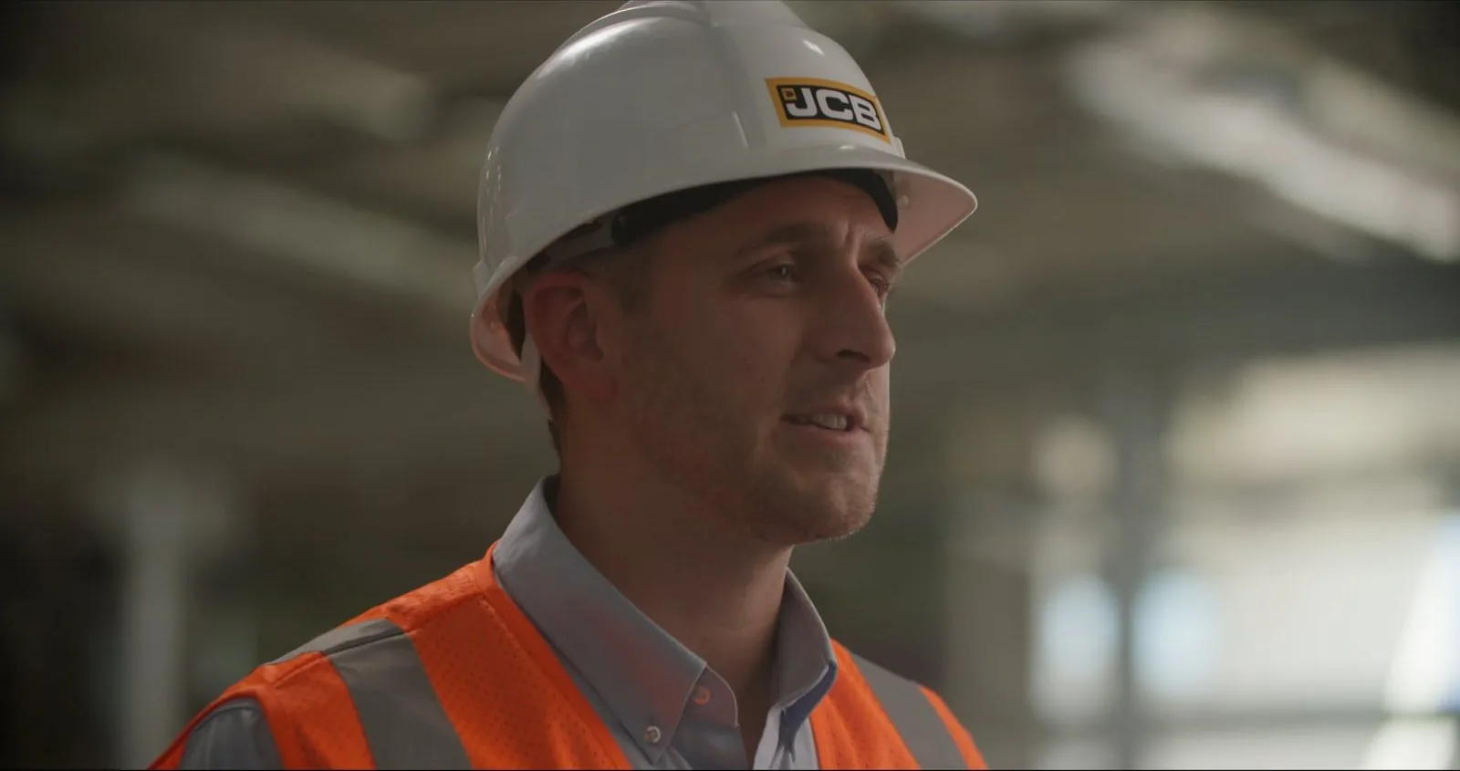 A JCB team member in a white hard hat and orange safety vest speaks during his interview.