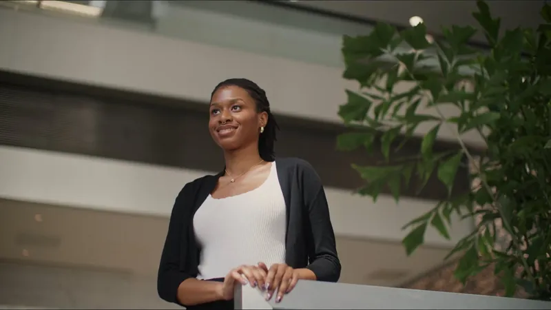 NPower alum Faith Uzo smiles by a railing in a bright office lobby.