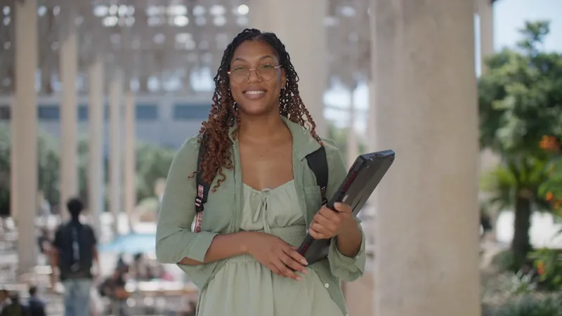 NPower alum Krivonne Evans smiles under a sunlit colonnade, a laptop under her arm.