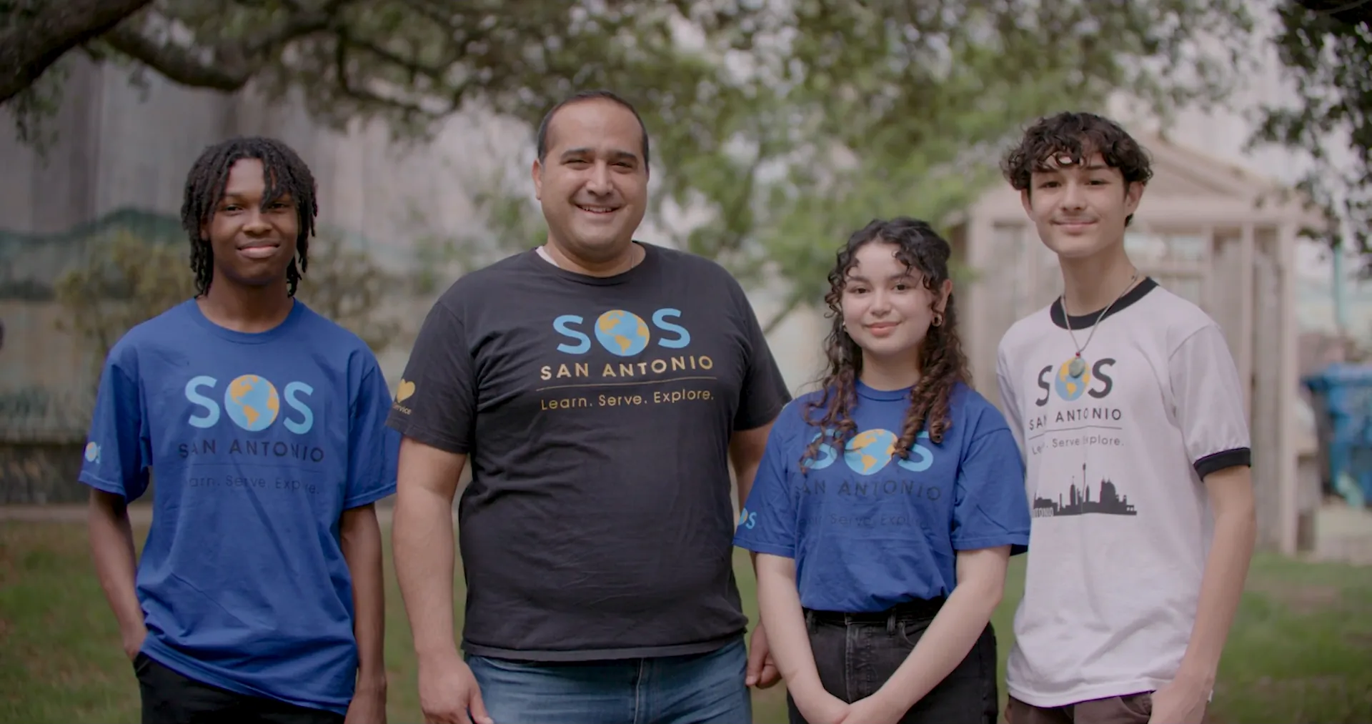 Students of Service founder Amir Samandi stands outdoors with three students in SOS San Antonio shirts.