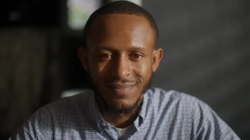 NPower alum Tahjee Speight, in a checked shirt, smiles in a close portrait.