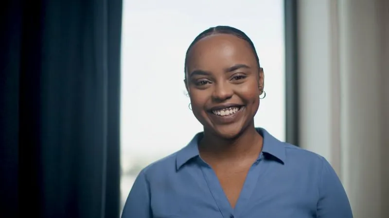 NPower Dallas alum Valentine Komen, in a blue shirt, smiles by a window.