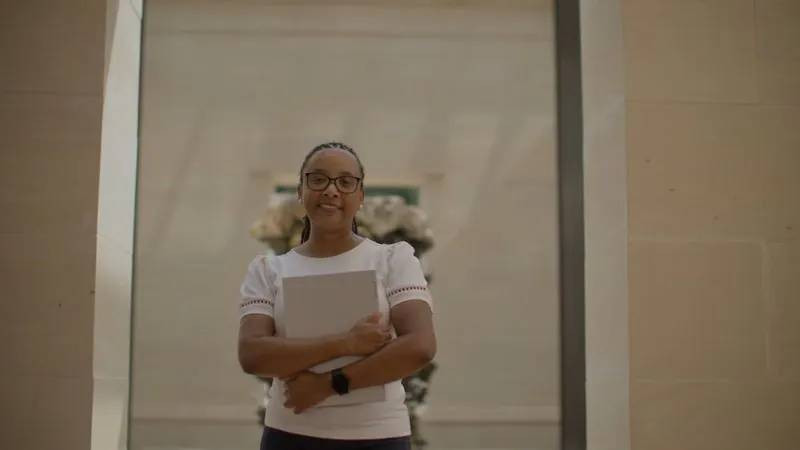 NPower alum Kayla Guillory stands in a hallway hugging a laptop to her chest.