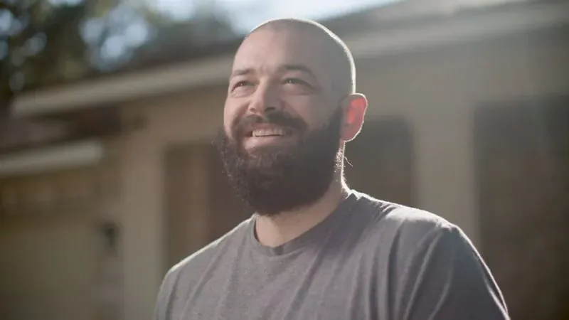 NPower alum Charlie Wright, in a gray T-shirt, smiles outdoors in warm afternoon light.