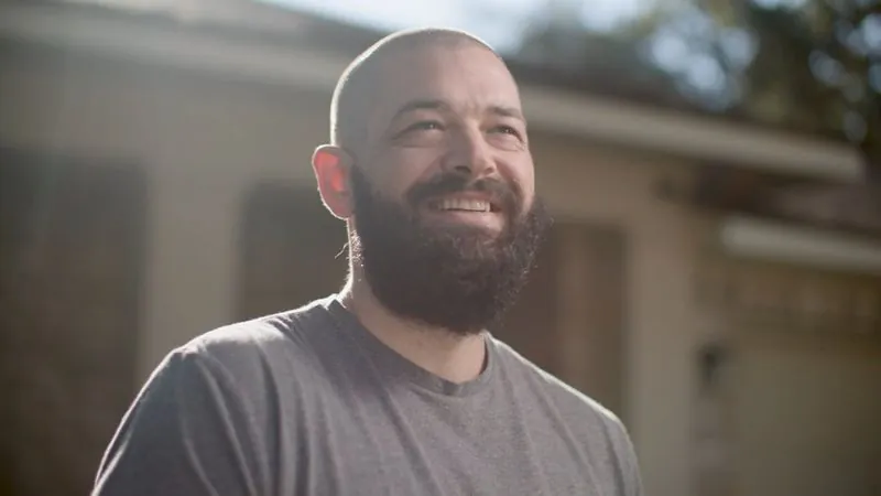 NPower alum Charlie Wright, in a gray T-shirt, smiles outdoors in warm afternoon light.