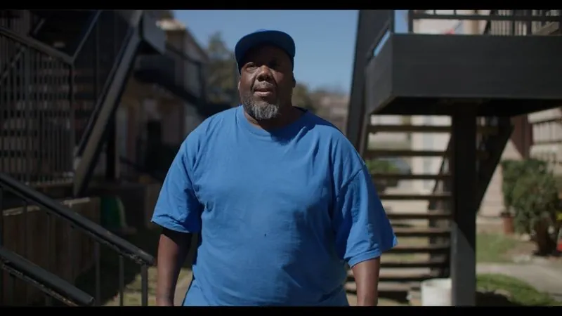 Scott Washington, in a blue T-shirt and cap, stands outside an apartment building.