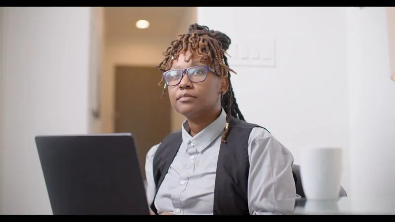 NPower alum Brittany Holmes, in glasses and a vest, sits at her laptop in a bright room.