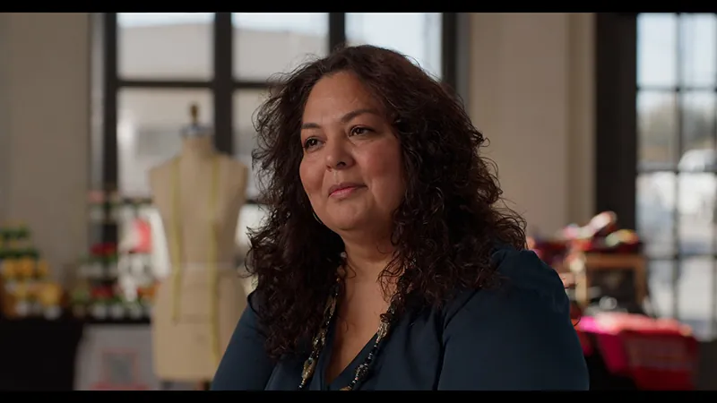A woman smiles during her interview beside a dress form at Basila Frocks.
