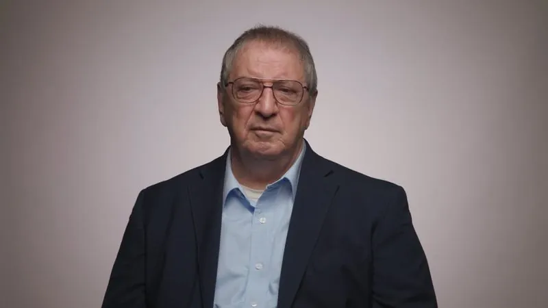 A man in a dark blazer and glasses sits for a legacy giving interview for the National Museum of the Pacific War.
