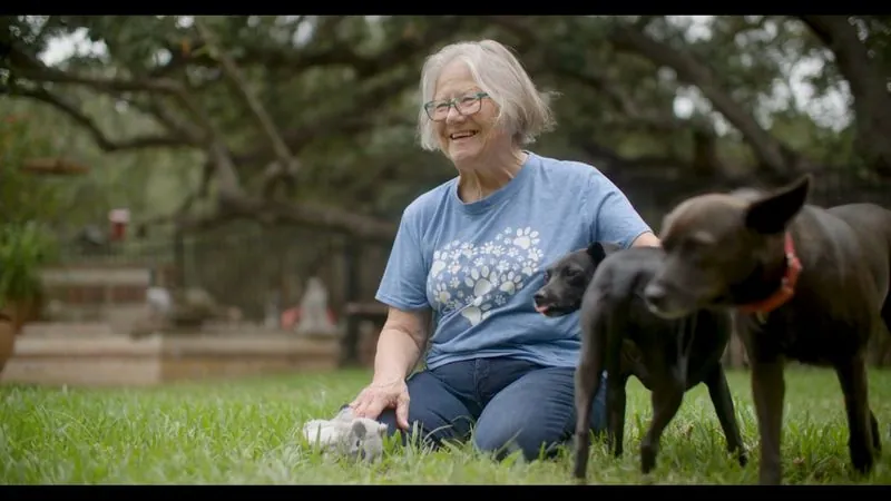 Peggy Gonzalez, San Antonio Pets Alive! Dog Foster of the Year, laughs on the grass with two dogs.