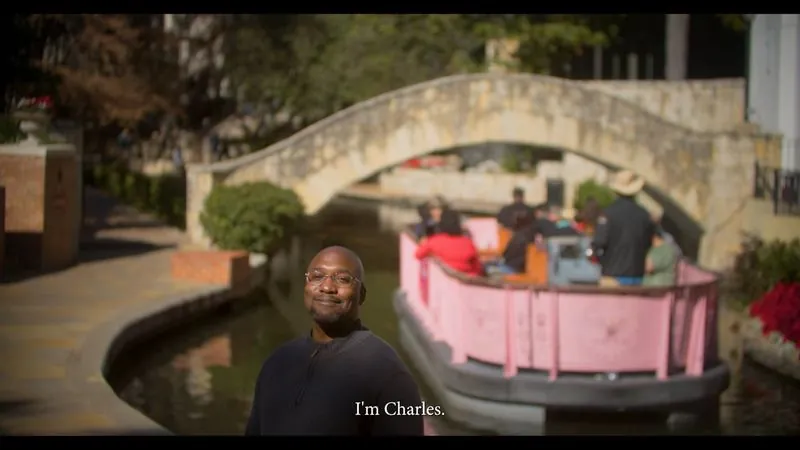 NPower San Antonio alum Charles Jones stands on the River Walk as a pink barge passes under a stone bridge.