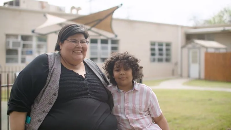 Libby and a young boy sit together on a lawn outside a building, from her SAMMinistries story.