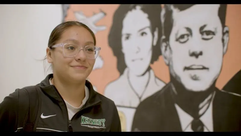 A Kennedy High School student smiles in front of a black and white mural.