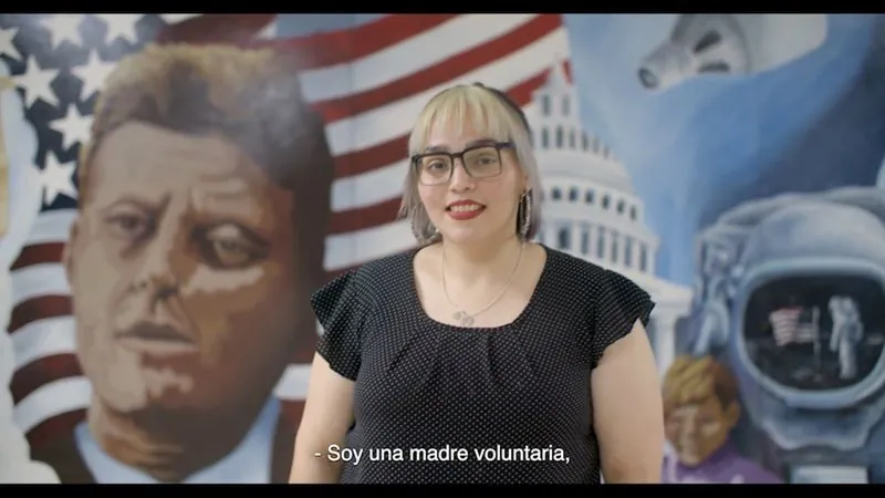 Parent volunteer Dora Maldonado speaks in front of a mural of John F. Kennedy at Kennedy High School.