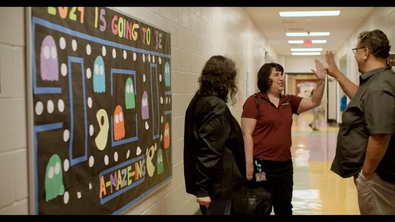 Educators trade a high five in an Edgewood ISD school hallway beside a Pac-Man bulletin board.