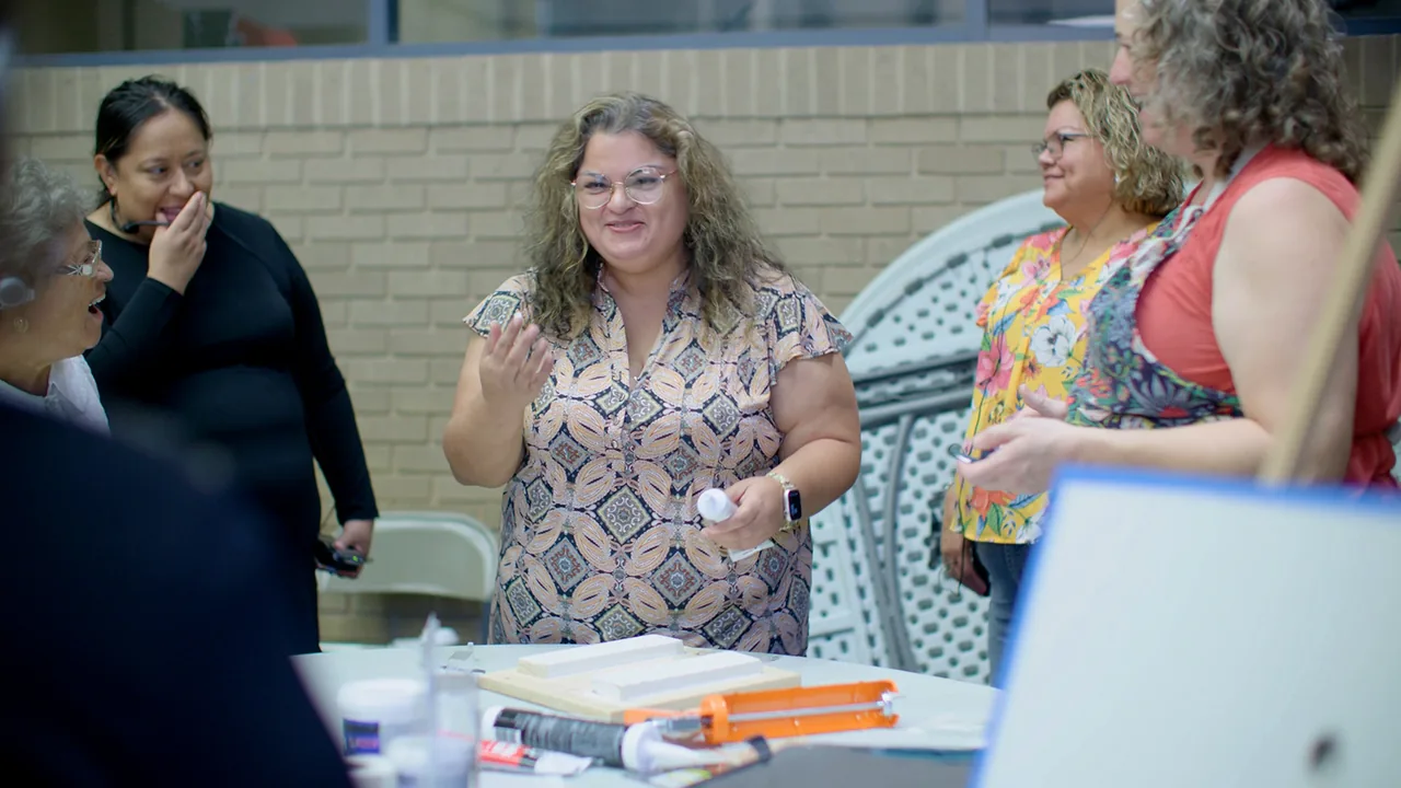 Women talk and laugh around a table at a community workshop, from our LISC San Antonio video.