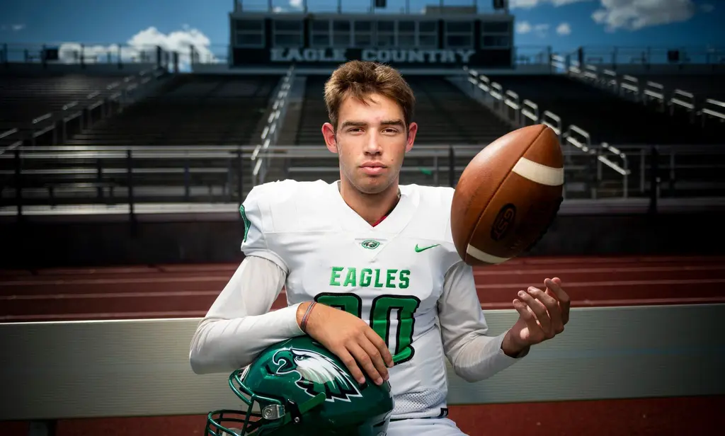 Eagles football player in a white jersey tossing a football and holding a green helmet at a stadium