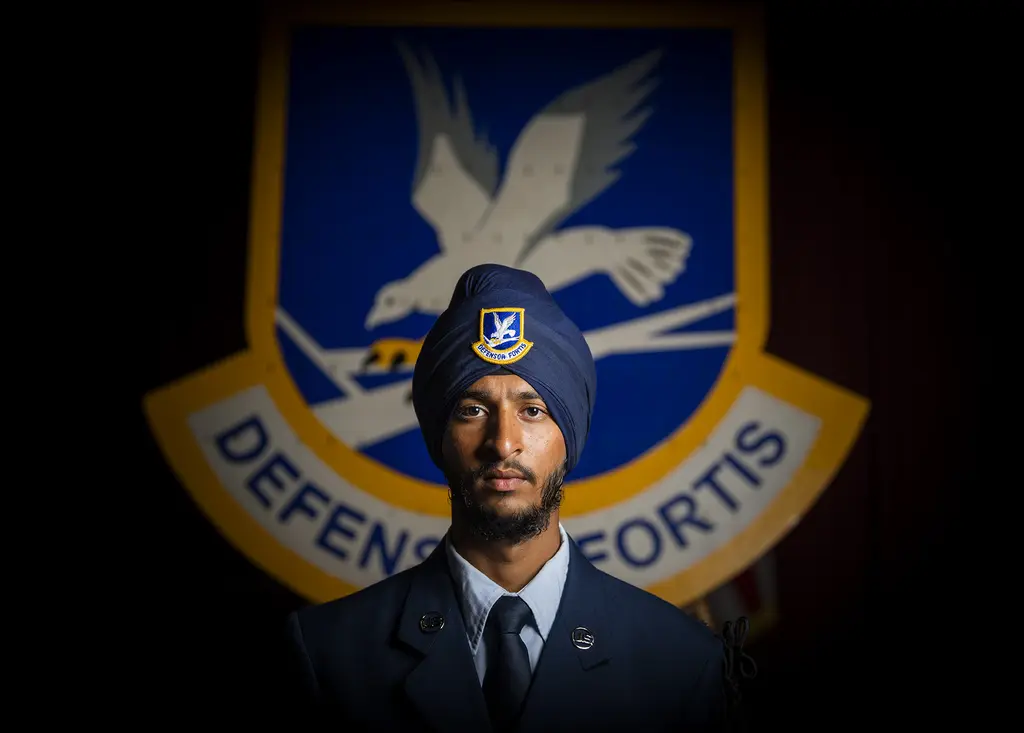 Airman Sunjit Rathour in a blue turban and Air Force uniform stands before the Security Forces Defensor Fortis shield