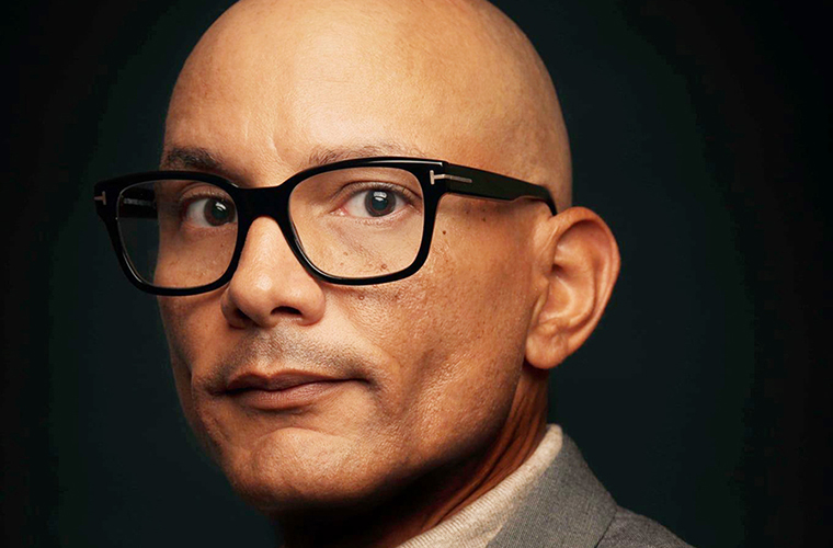 Carlos Javier Sanchez, founder and chief creative officer of pixelreflex MEDIA, in black-framed glasses and a gray blazer, in a close-up color portrait.