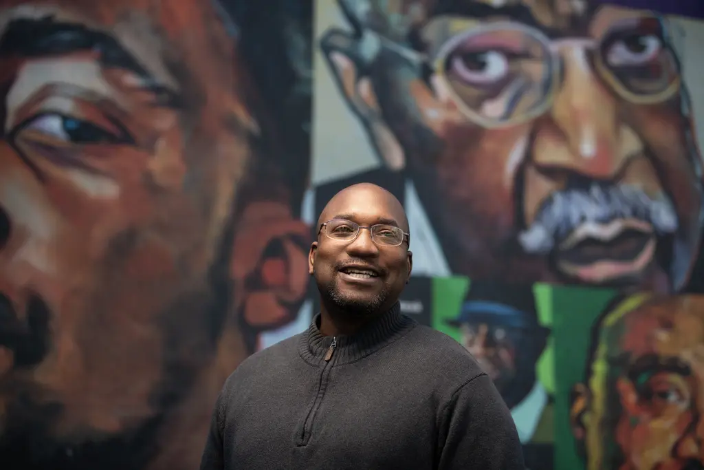 Charles Jones smiling in front of a colorful mural of large painted portraits of Black men