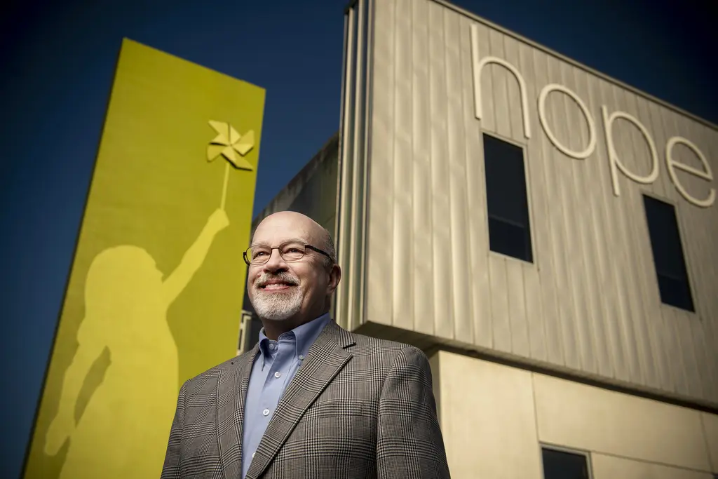 Fred Hines in glasses and a tweed jacket outside a building marked "hope" beside a mural of a child with a pinwheel