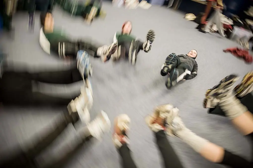 Women's crew rowers lie in a circle on a carpeted floor with legs raised, blurred by a spinning camera