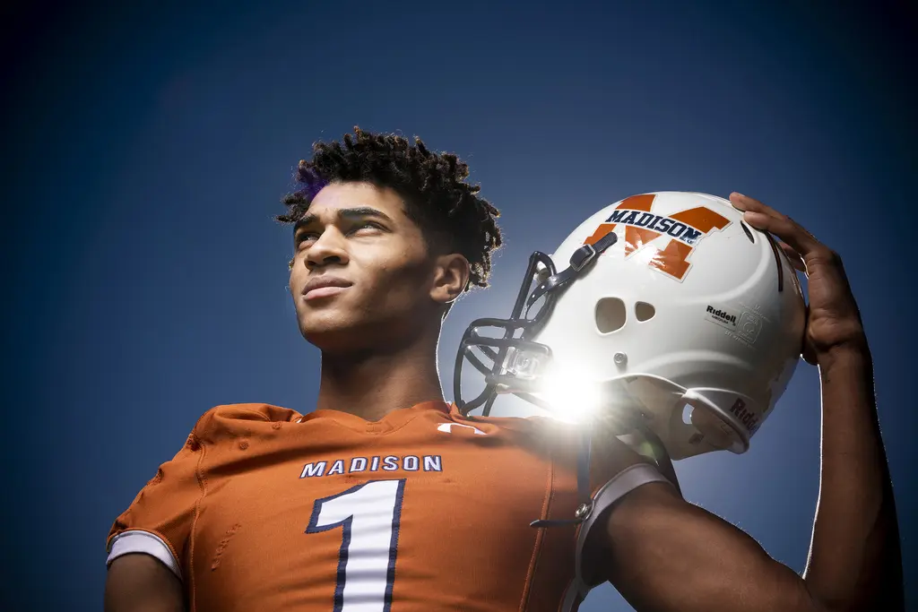 Dante Heaggans in an orange No. 1 Madison jersey holds his white helmet against a deep blue sky