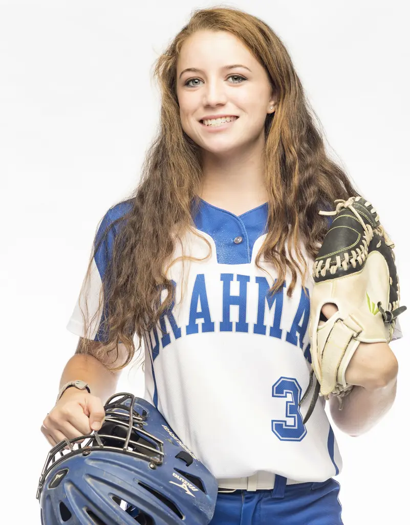 Kindell Brooks in a white and blue Brahmas softball jersey holds a catcher's mitt and helmet