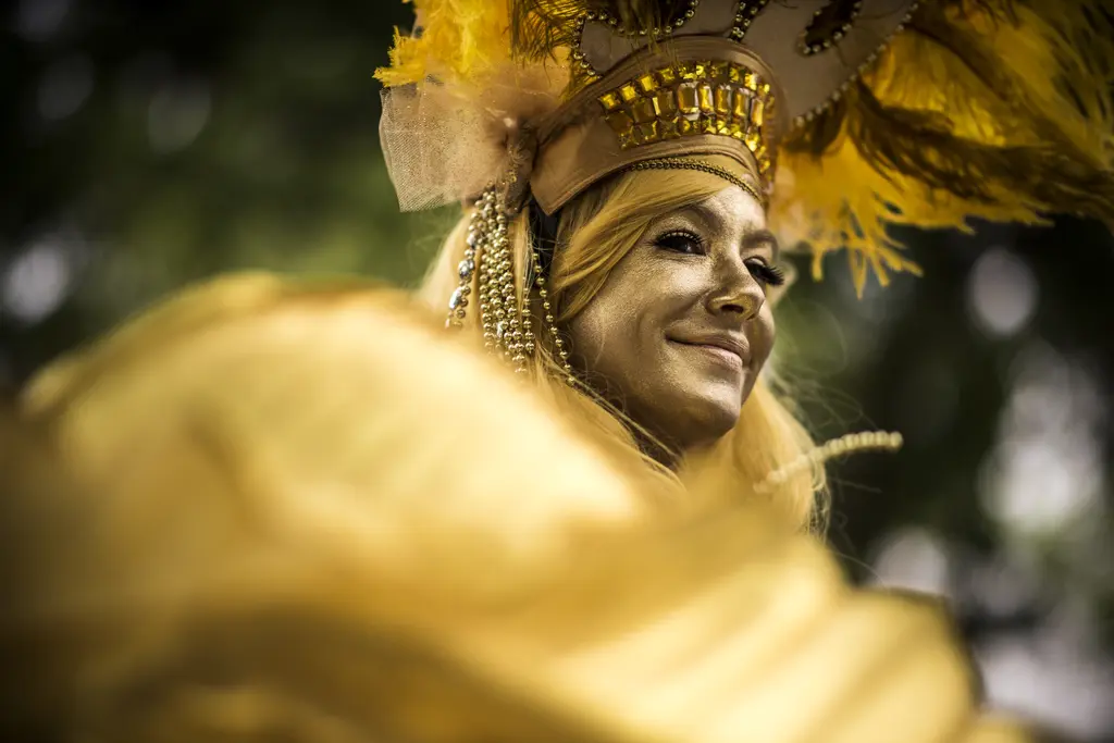 Performer in gold face paint and a feathered gold headdress smiling at the King William Parade in San Antonio