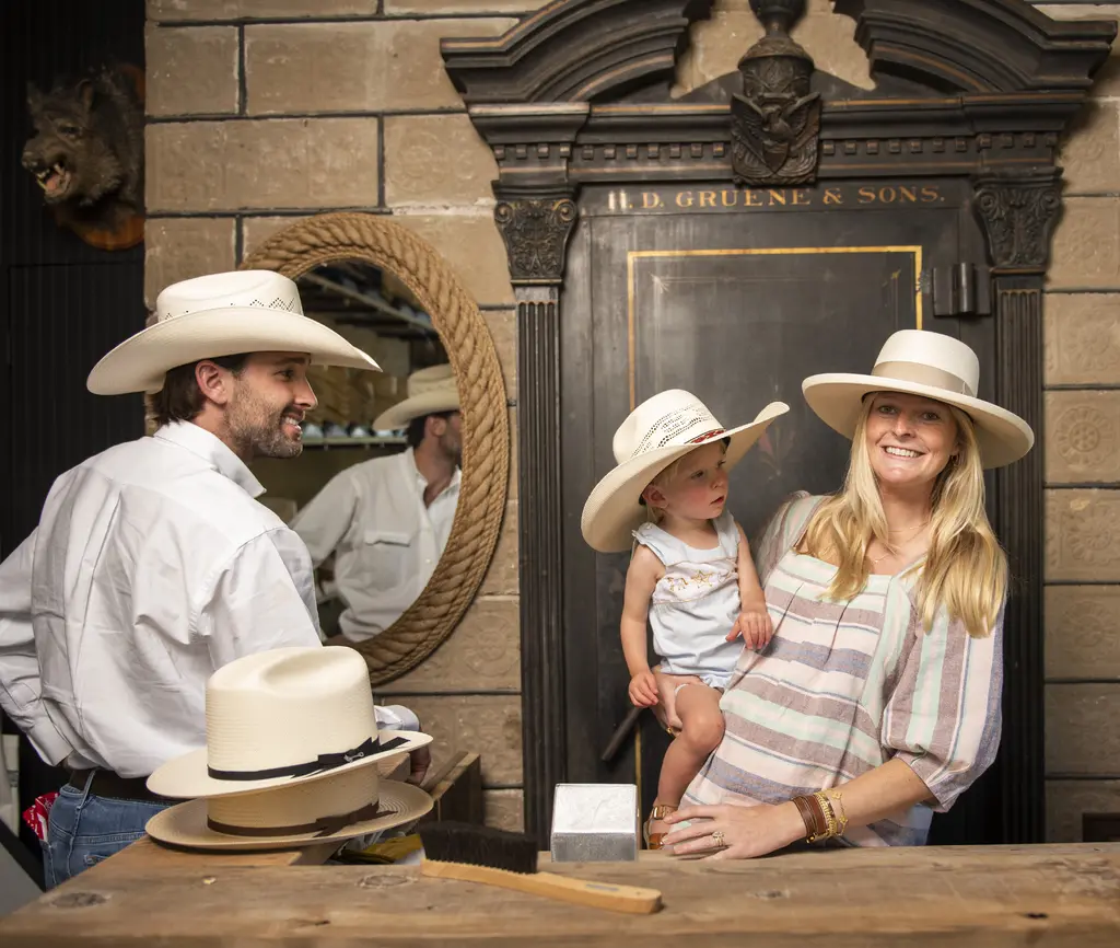 Cody Courtney in a cowboy hat smiling at Katie Courtney and a toddler in straw hats inside Gruene Hat Company
