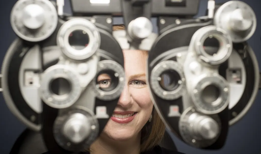 Dr. Lisa Marten smiling, one eye peering through the lenses of a phoropter