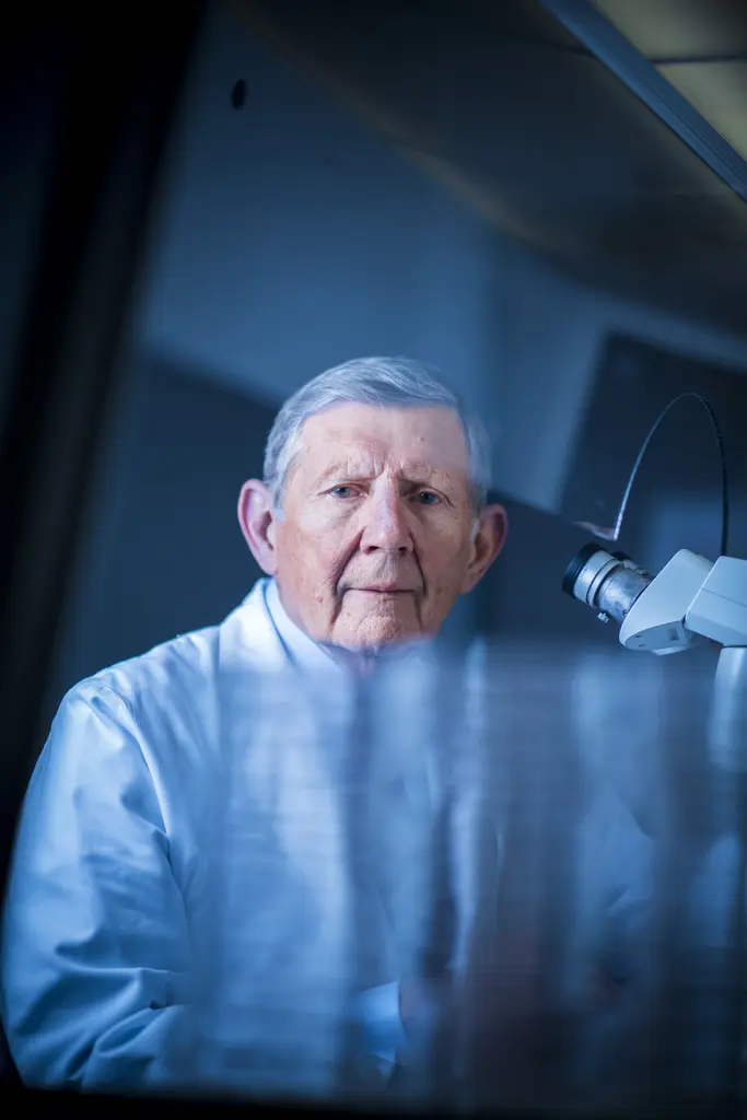 Dr. Joseph E. Martin in a light blue shirt, seen through glass beside a laboratory microscope
