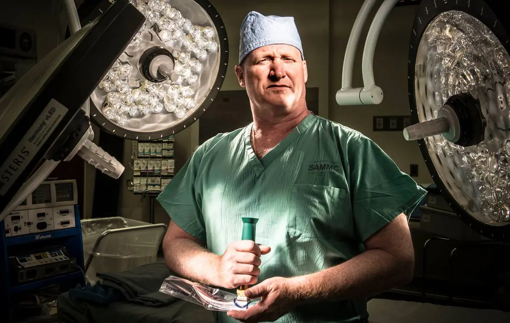 Col. Joseph Brennan in green scrubs and a surgical cap holding a laryngoscope under operating room lights