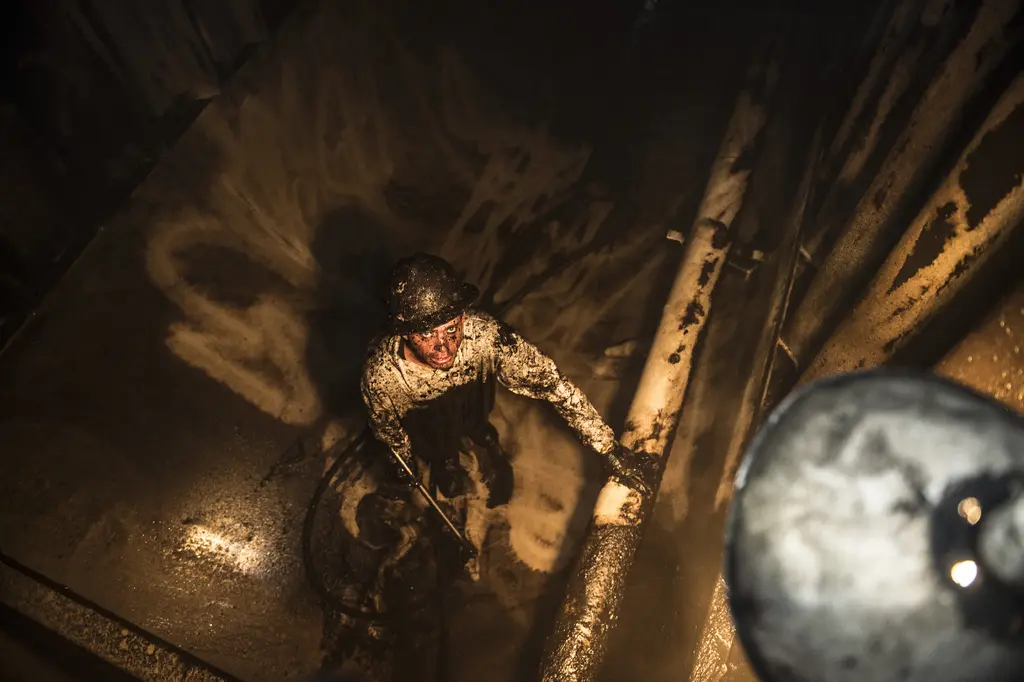 Adam Morris, coated in mud, cleaning the inside of a fracking tank with a hose