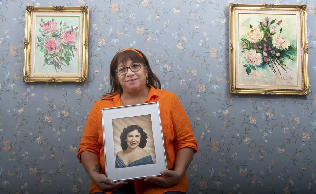 Cindy Mills Sowers in an orange shirt holds a framed vintage portrait in front of floral wallpaper
