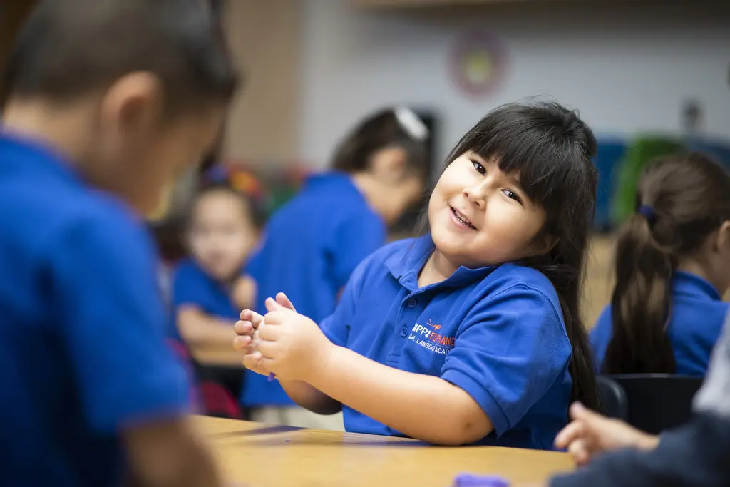 Smiling girl in a blue KIPP Esperanza polo shaping purple clay at a classroom table
