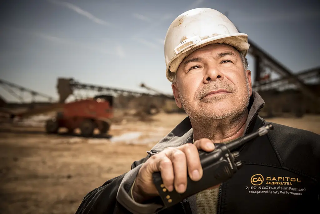 Capitol Aggregates worker in a white hard hat holding a two-way radio at an aggregates plant