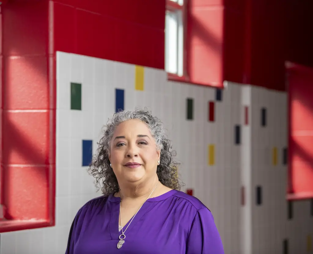 Celeste Martinez in a purple blouse in front of red walls and white tile with colored accents