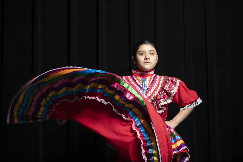 Folklorico dancer in a red ribbon-trimmed dress swirling her skirt against a black curtain