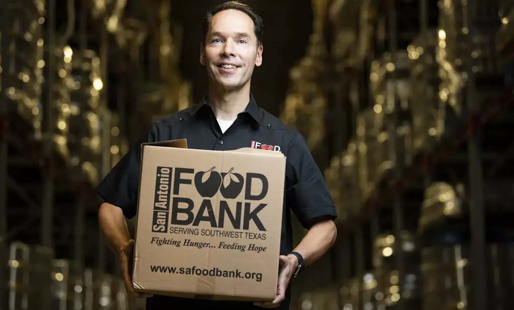 Eric Cooper smiling and holding a San Antonio Food Bank box in a warehouse aisle