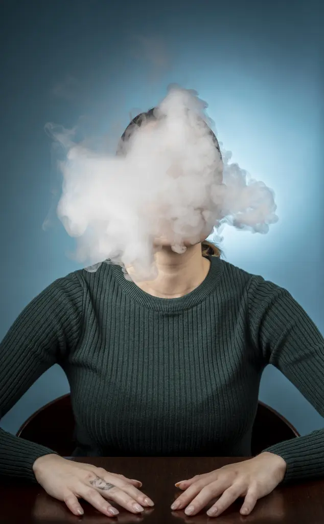 Photo illustration of a woman in a green sweater at a table, her face hidden by a cloud of vapor.